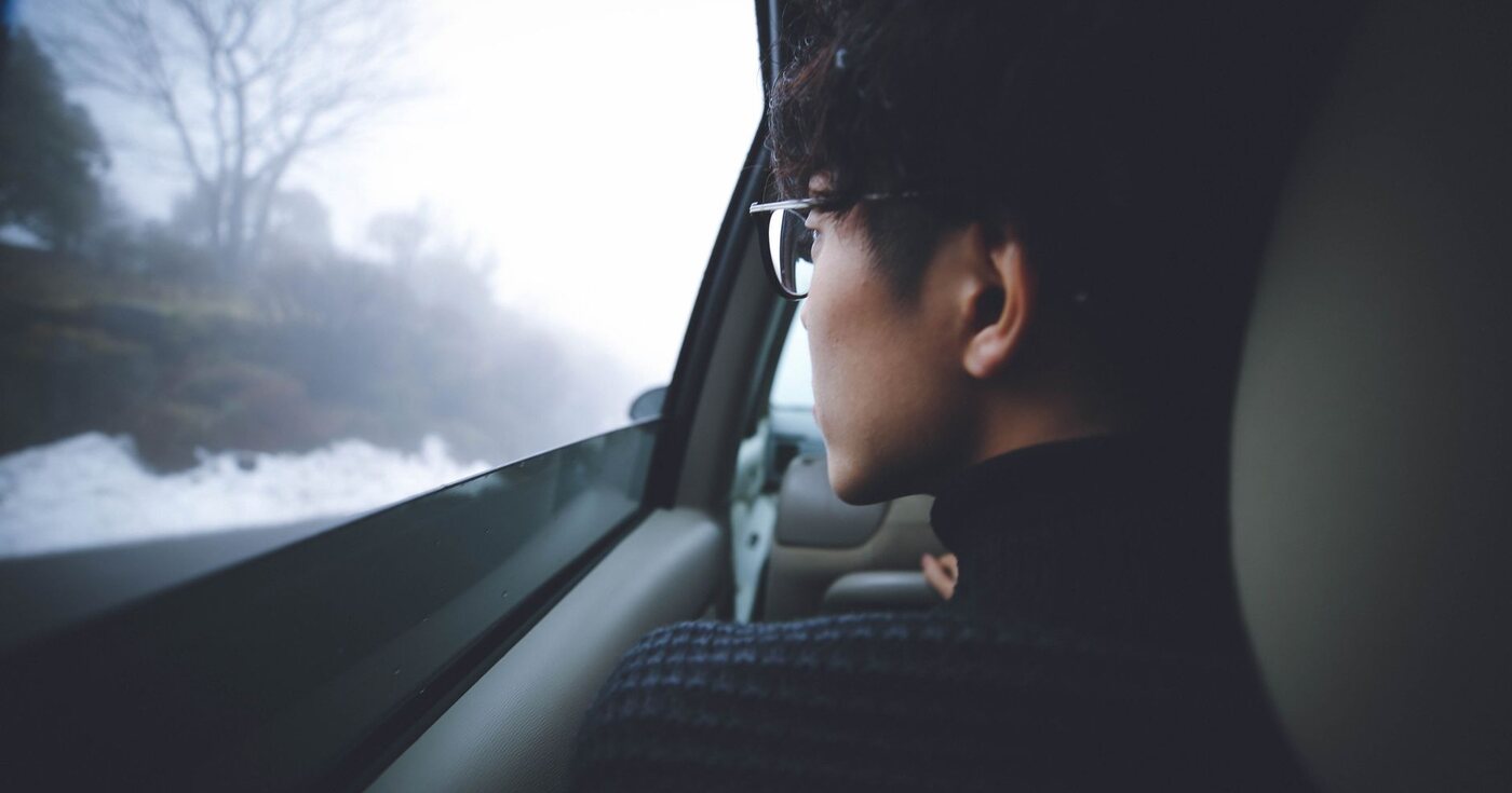A thoughtful person looking through a car window at a foggy landscape