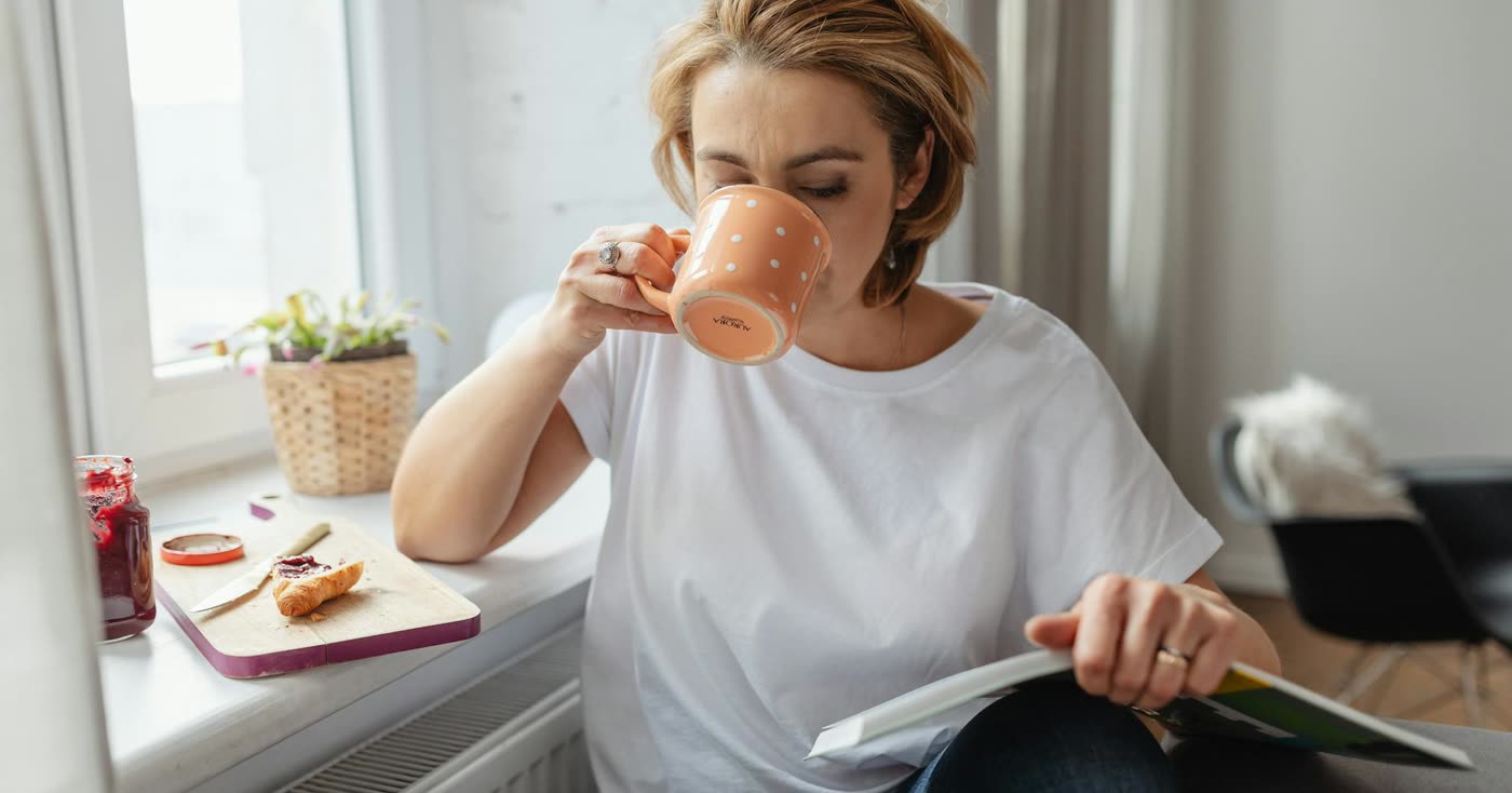 A woman reading with morning coffee by a bright window, building a new smoke-free routine