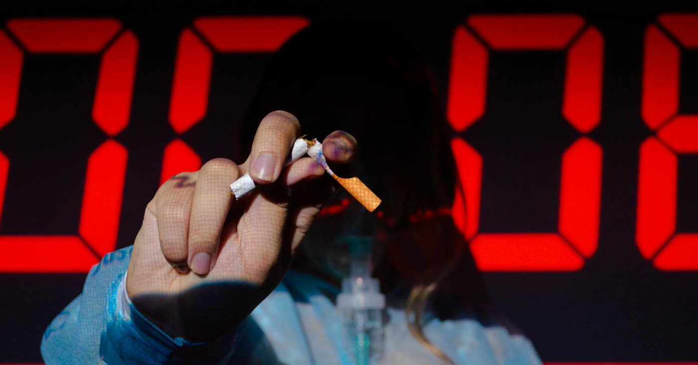 A hand holding a broken cigarette beside a timer, marking the first smoke-free day