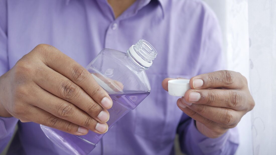A person pouring purple mouthwash into its bottle cap